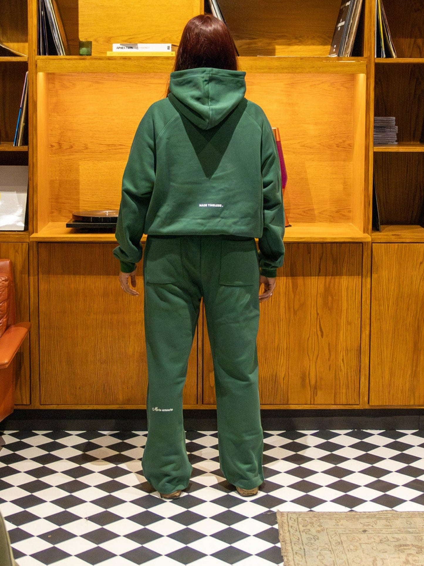 Person in green outfit standing in front of a wooden bookshelf with vinyl records.