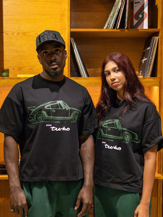 Two people wearing black t-shirts with a car design in front of a wooden shelf.
