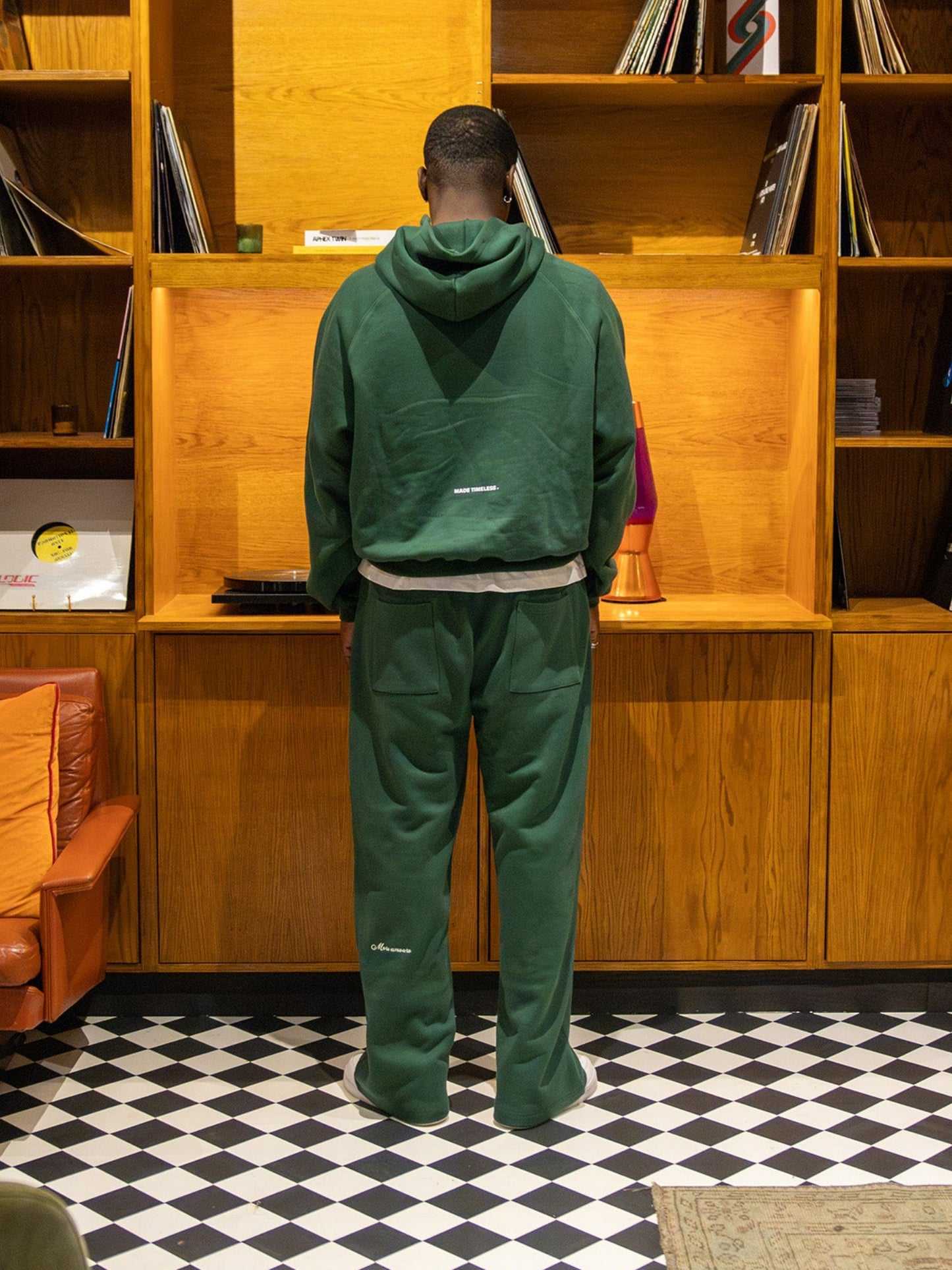 Person in green tracksuit standing in front of a wooden bookshelf with vinyl records.