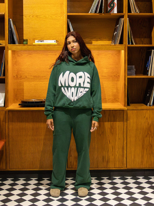 Person wearing a green hoodie with 'MORE AMOURE' text in a room with wooden shelves and vinyl records.