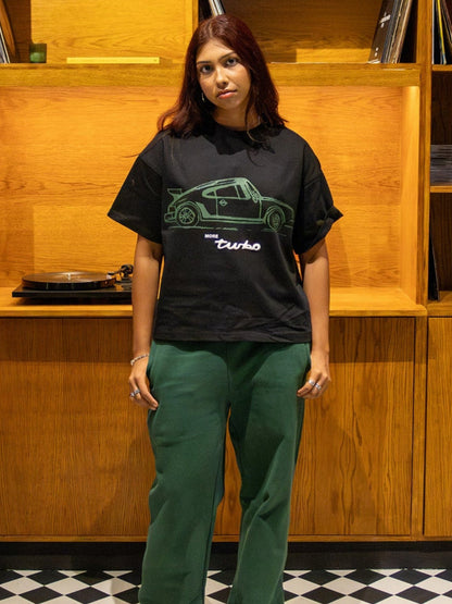 Person wearing a black t-shirt with a graphic design in a room with wooden bookshelves and checkered floor.